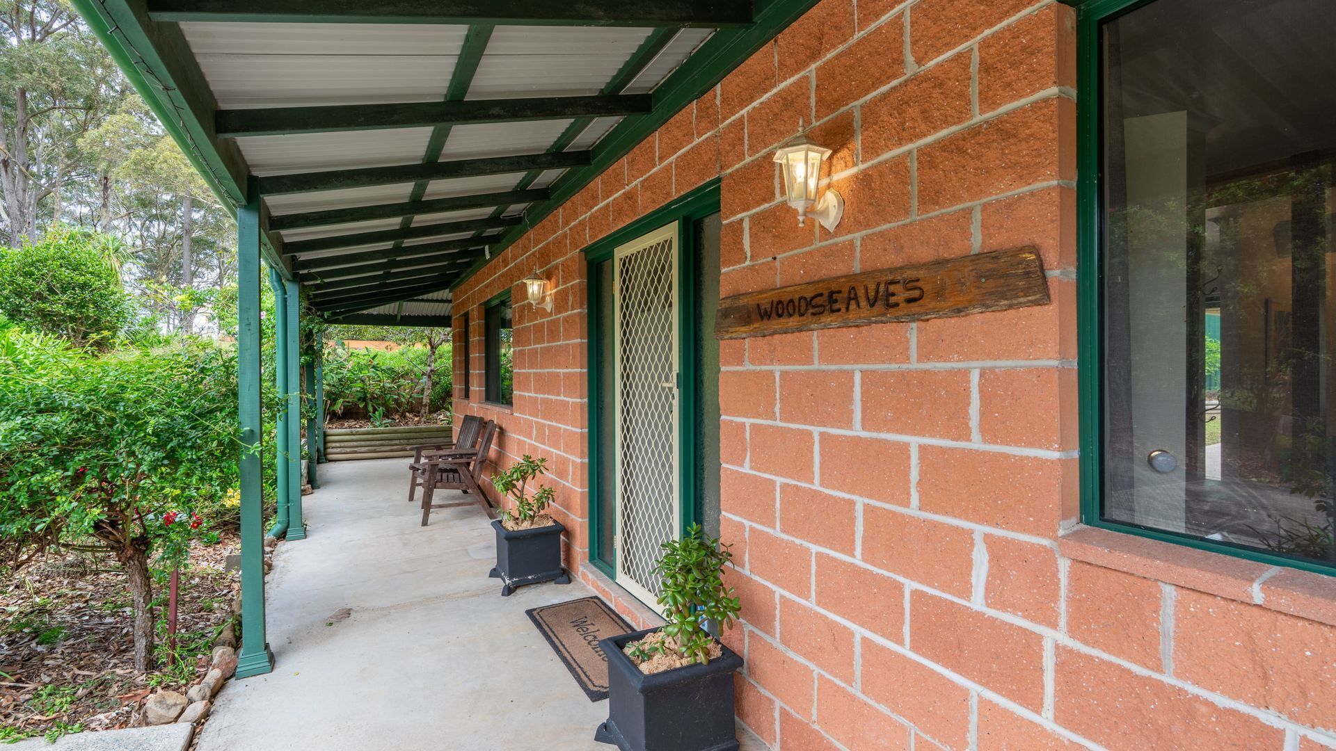 A covered porch with brick walls, a wooden sign reading "WOODS AVES", and potted plants.