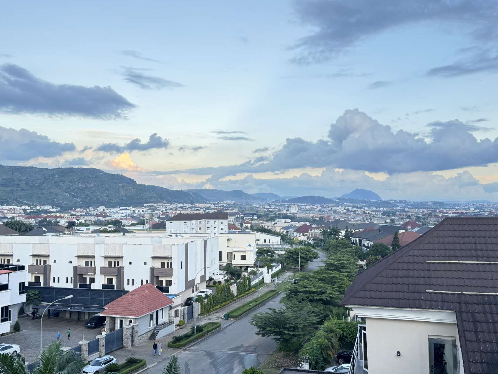 A residential area with modern buildings, a clear sky, and distant mountains.