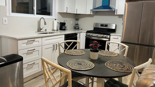 Uma cozinha moderna com armários brancos, uma geladeira de aço inoxidável, um fogão e uma mesa de jantar com jogos americanos de palha.