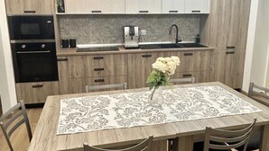 Une cuisine moderne avec des meubles en bois, un four encastré, une machine à café et une table à manger avec des chaises.