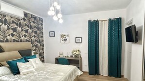 Une chambre à coucher avec un lit, un bureau, une chaise, une télévision et une fenêtre avec des rideaux.