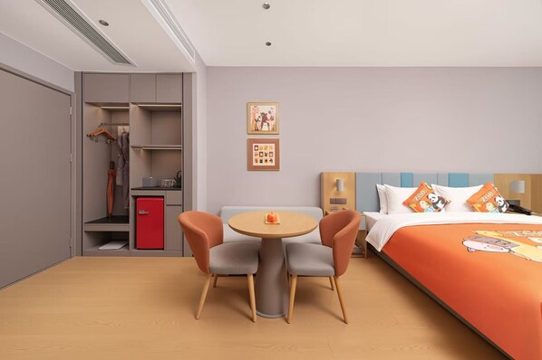 Une chambre d’hôtel comprenant un lit, un bureau, deux chaises, une petite table, une armoire et un mini-réfrigérateur rouge.