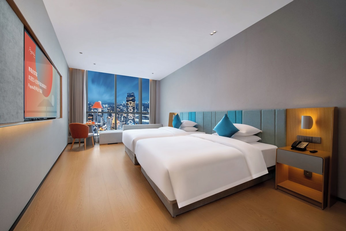 Una habitación de hotel moderna con dos camas, vistas a la ciudad, un escritorio y una silla.