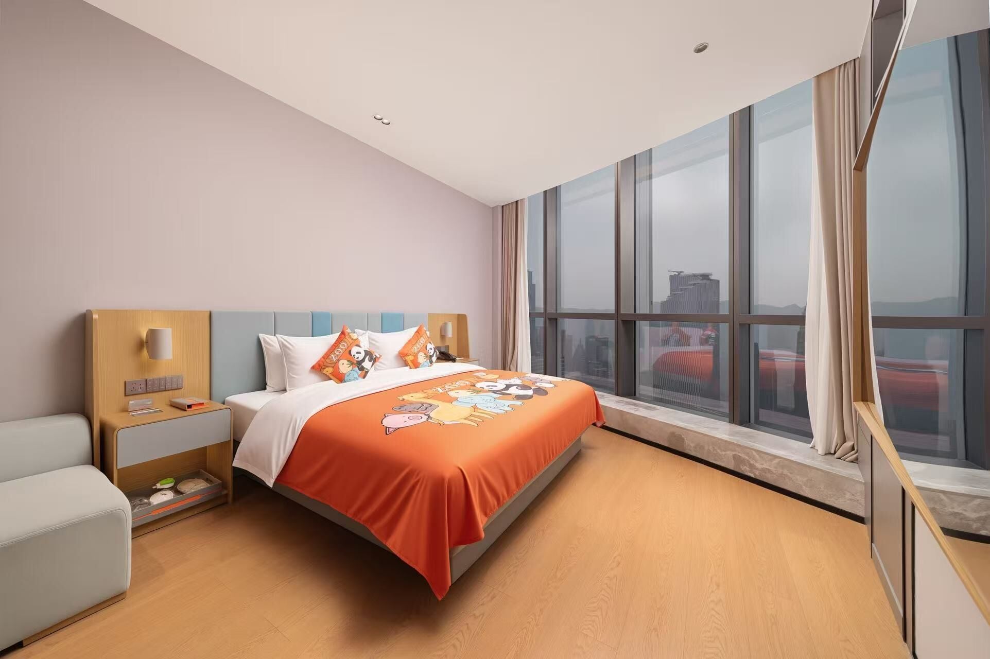 A modern hotel room with a large bed, a bedside table with a lamp, a small sofa, and a large window offering a city view.