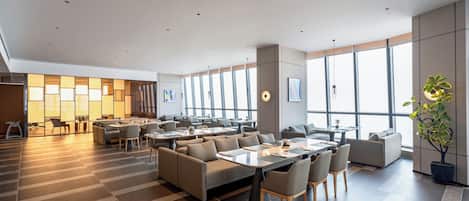 A spacious hotel lobby with multiple seating areas, large windows, and a modern design.