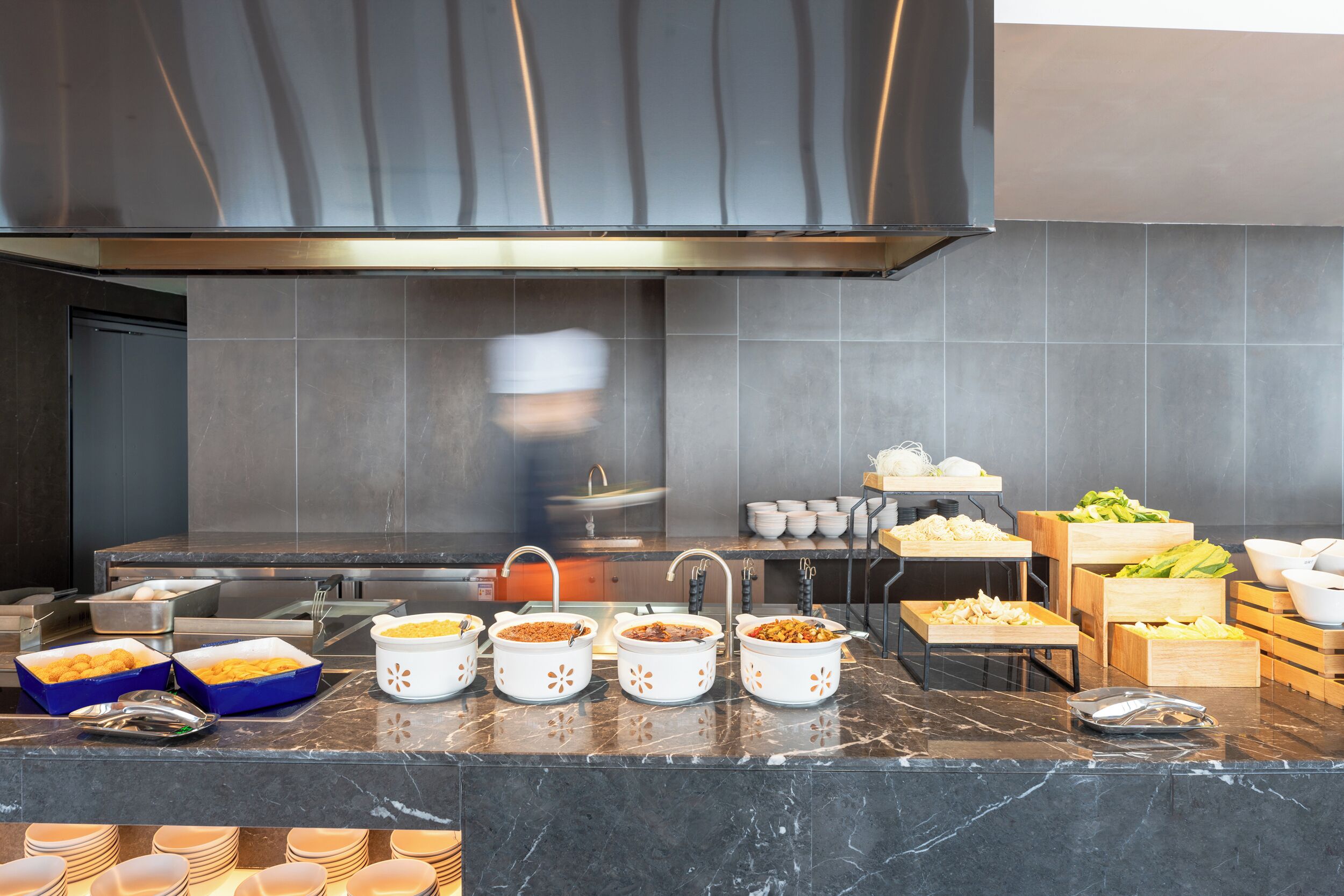 A modern kitchen with marble countertops, various food containers, and a large exhaust hood.