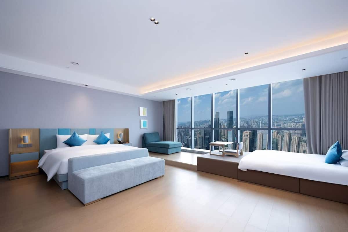 A modern hotel room with two beds, a sofa, a small table, and a city view.