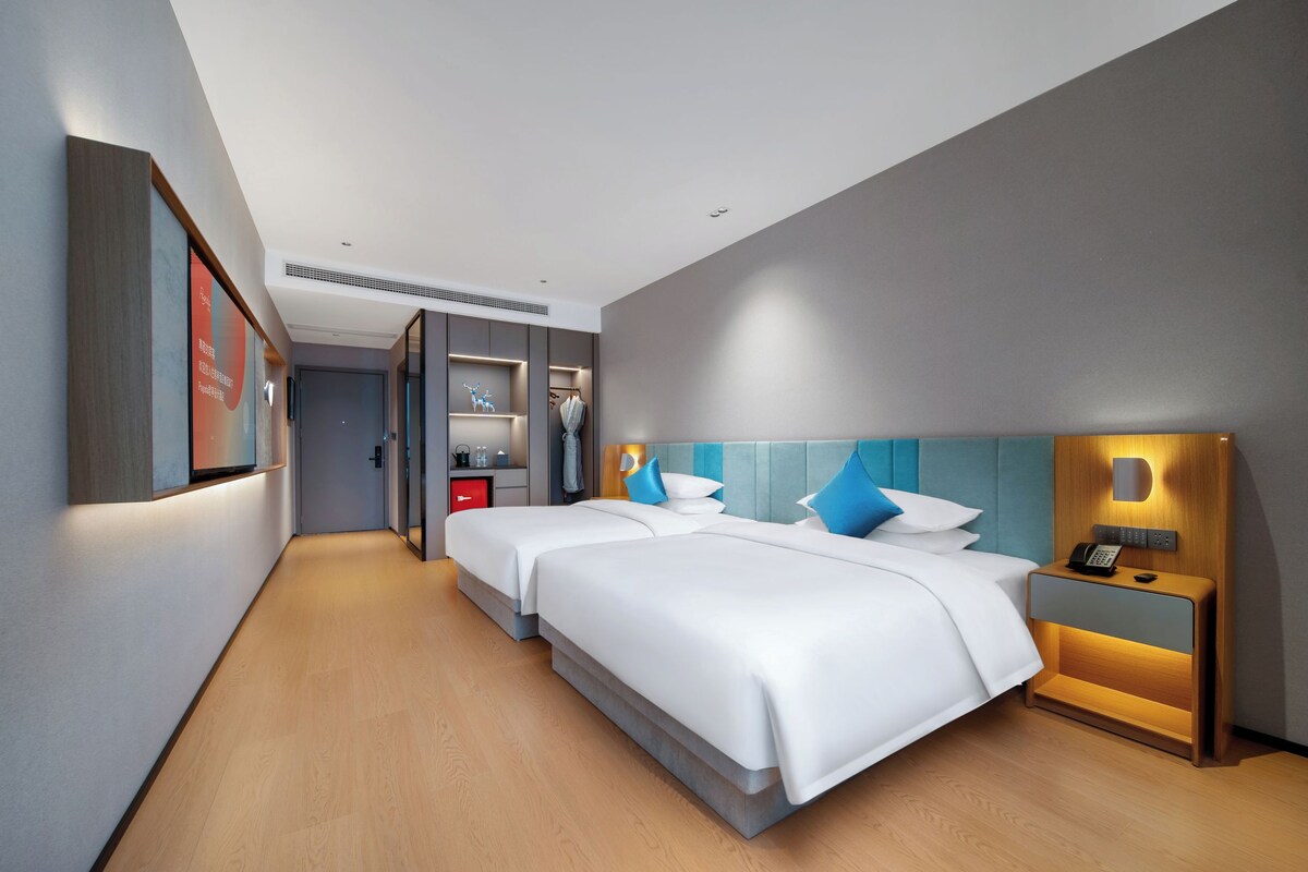 Una habitación de hotel moderna con dos camas, una mesita de noche con teléfono y un pequeño escritorio con lámpara.
