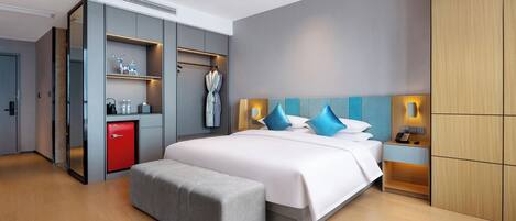 Een moderne hotelkamer met een groot bed, een grijze bank, een rode minibars kast en een garderobe met spiegel.