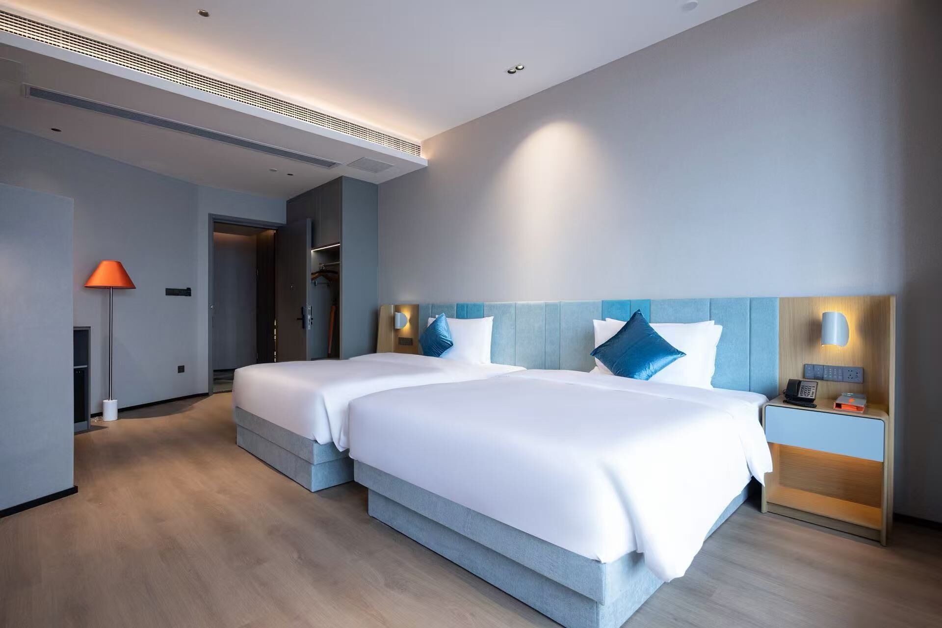 Et moderne hotelværelse med to senge, et walk-in closet, et natbord med telefon og lampe.