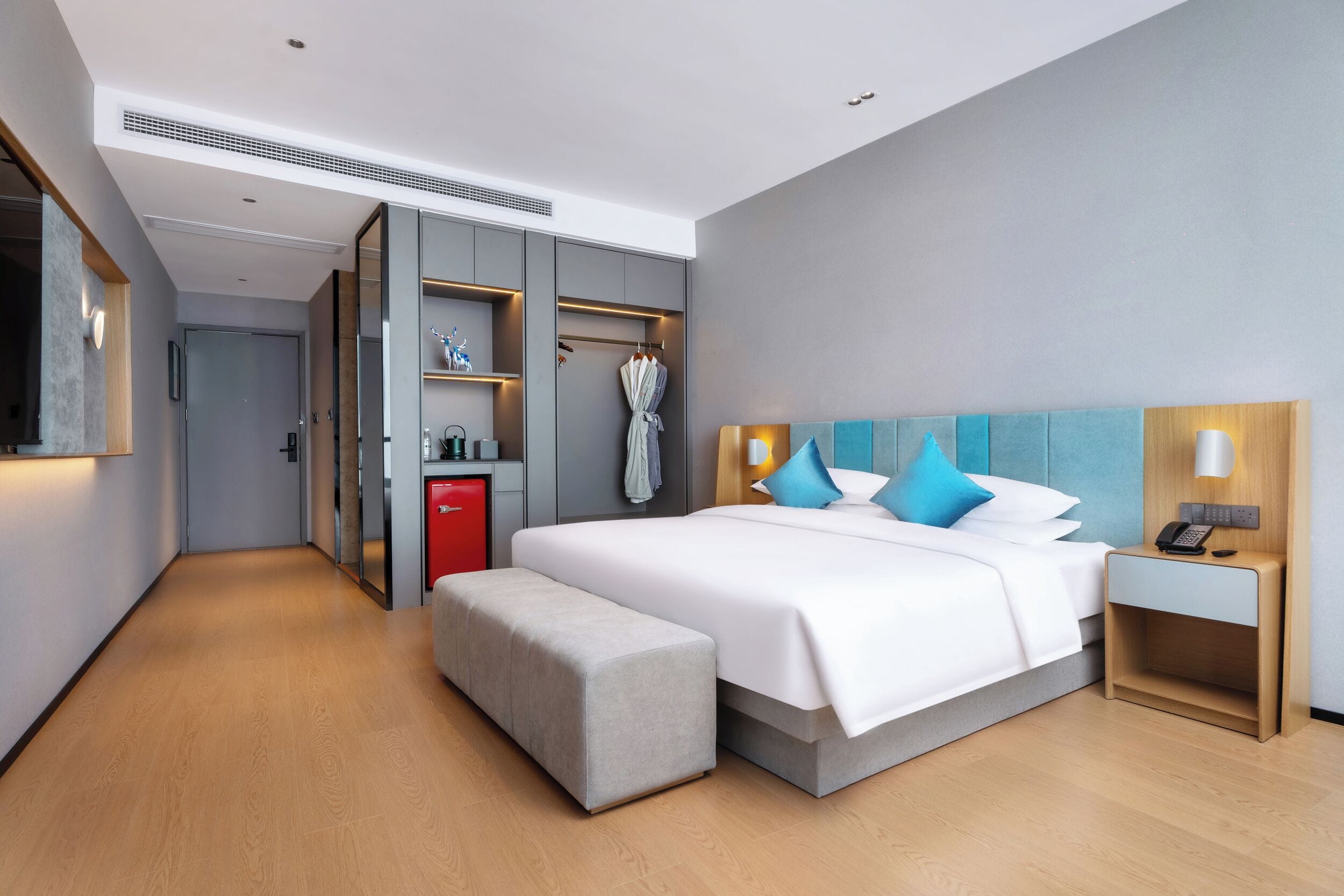 Una habitación de hotel moderna con una cama grande, una mesita de noche con lámpara, un armario y un banco.
