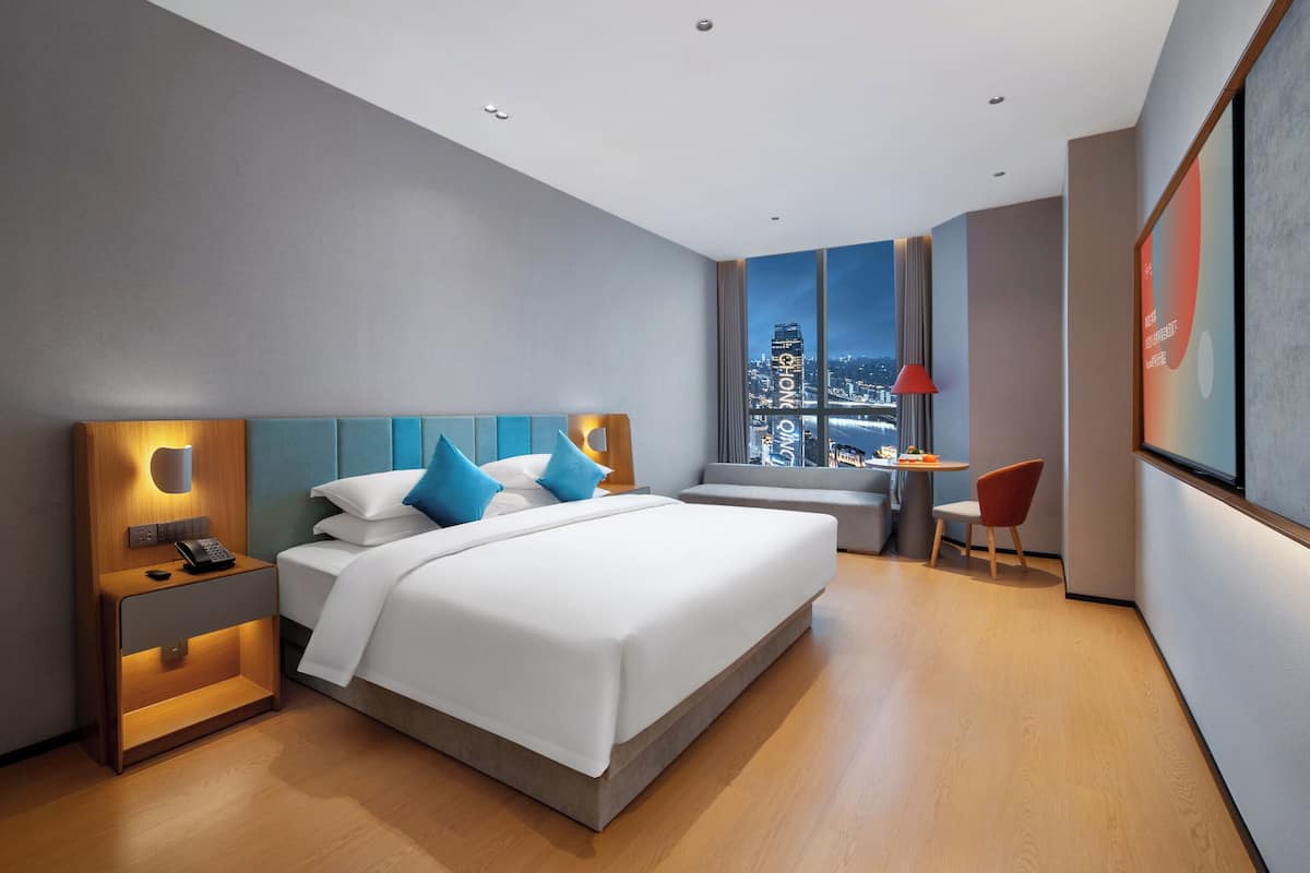 A modern hotel room with a large bed, bedside tables, a desk, and a chair.