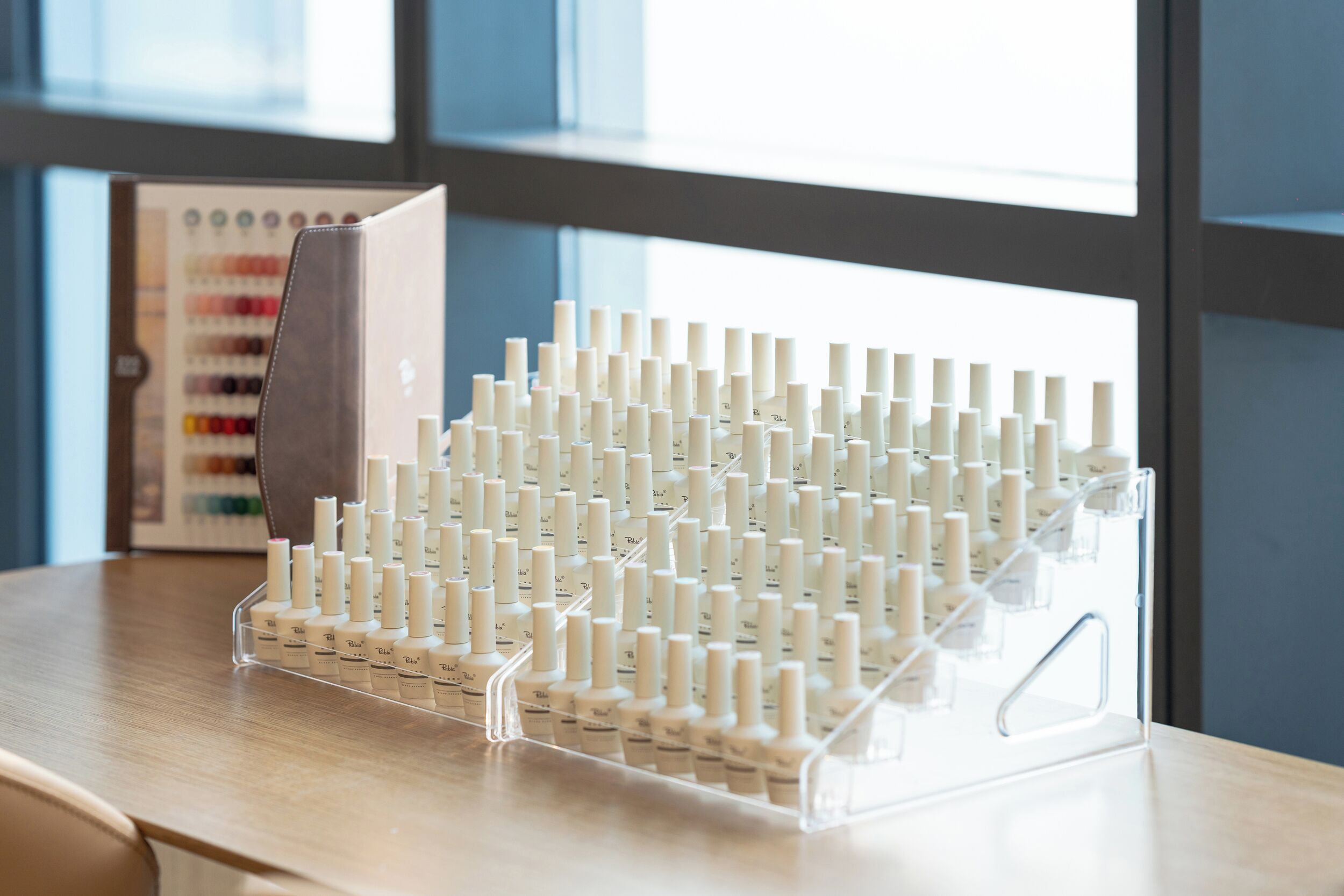 A clear plastic display stand holding multiple bottles of a product, likely a skincare or cosmetic item, on a wooden surface.
