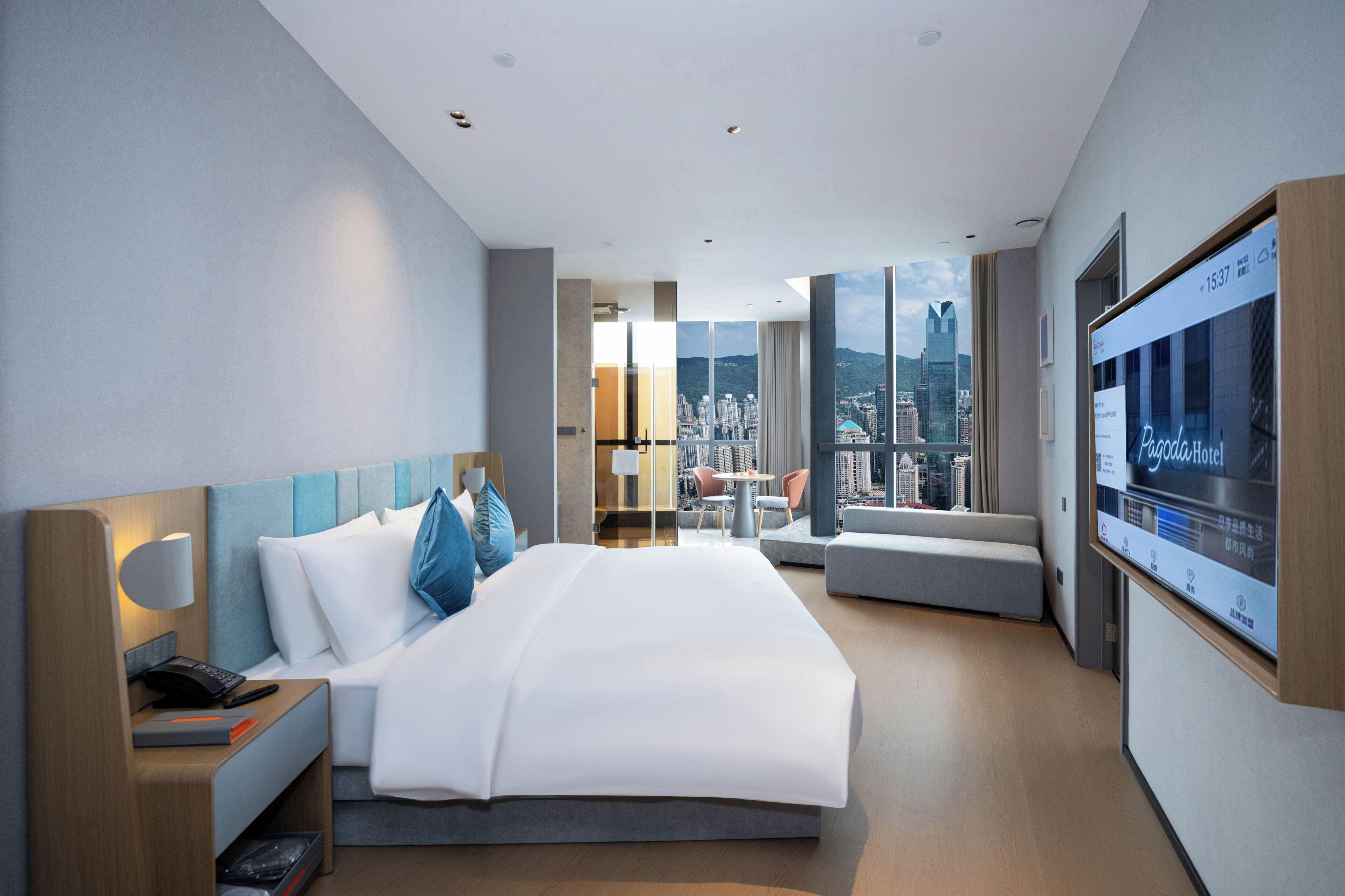 Habitación de hotel moderna con una cama grande, un escritorio con teléfono, televisor y vistas a la ciudad.