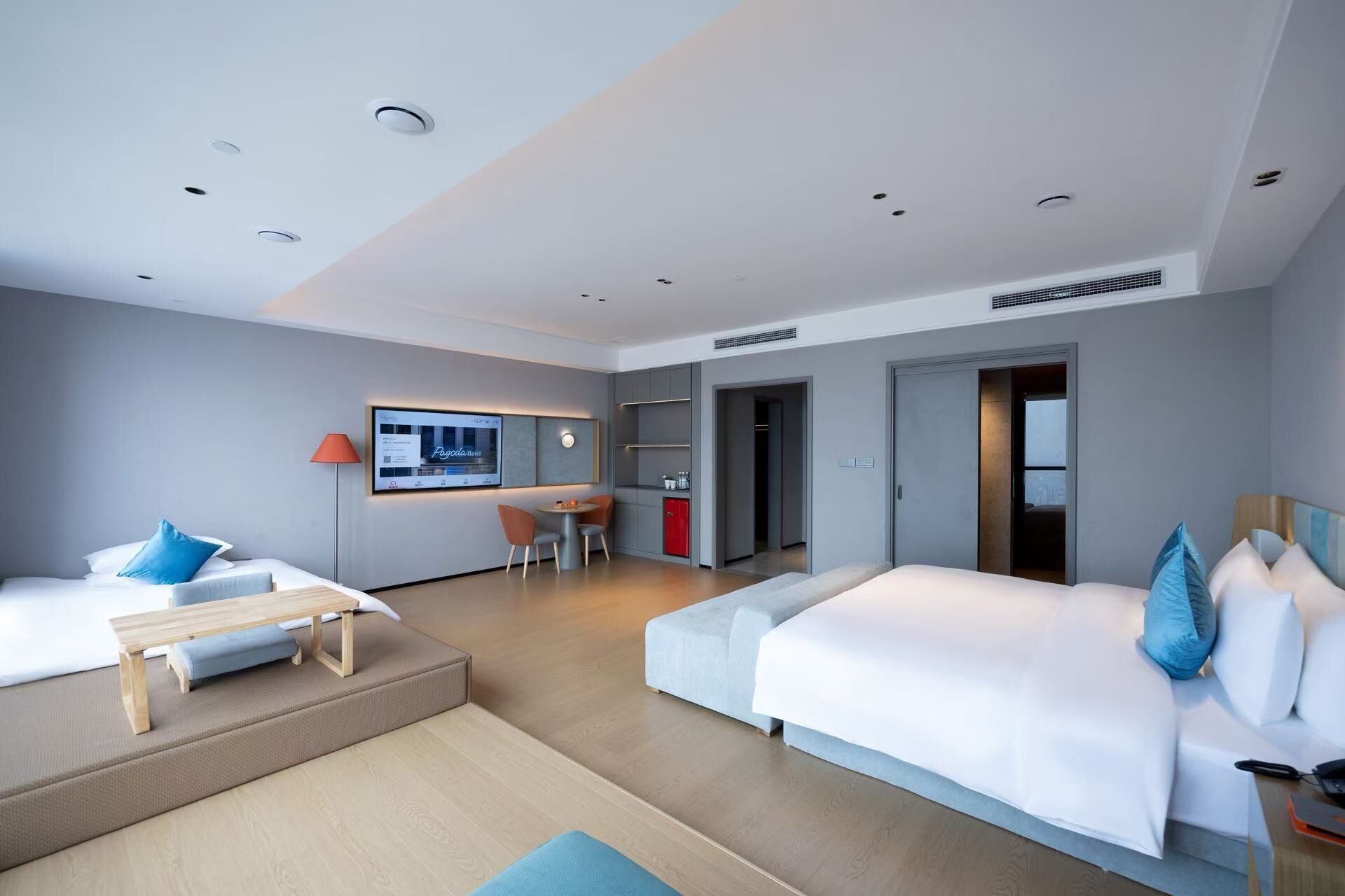 A modern hotel room with two beds, a desk, and a seating area.