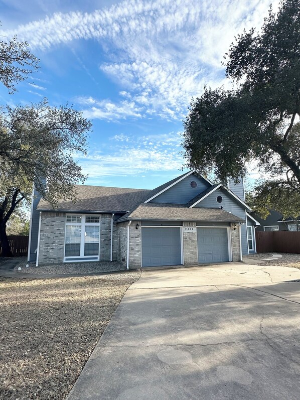A two-story house with a garage, a brick exterior, and a large tree to the left. - Prime NW Austin TX near Domain, Apple, Oracle, high tech corridor upgraded home! (Austin)