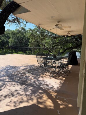 An outdoor patio with a table and chairs, a ceiling fan, and a view of a tree-lined area. - Beautiful yard with TONS of waterfront! (Kingsland)