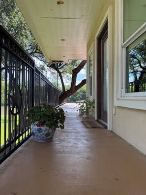 A covered porch with a potted plant, a metal fence, and a large tree. - Beautiful yard with TONS of waterfront! (Kingsland)