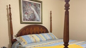 A four-poster bed with a floral bedspread and a yellow blanket, a wooden nightstand, and a framed picture on the wall.
