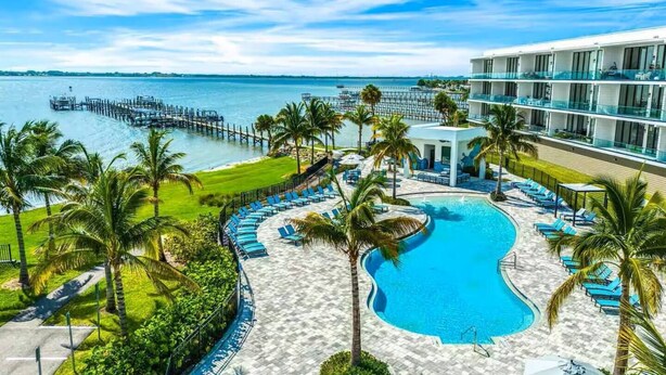 Ein Resort mit Schwimmbad, Palmen und einer Steg, der ins Wasser führt.