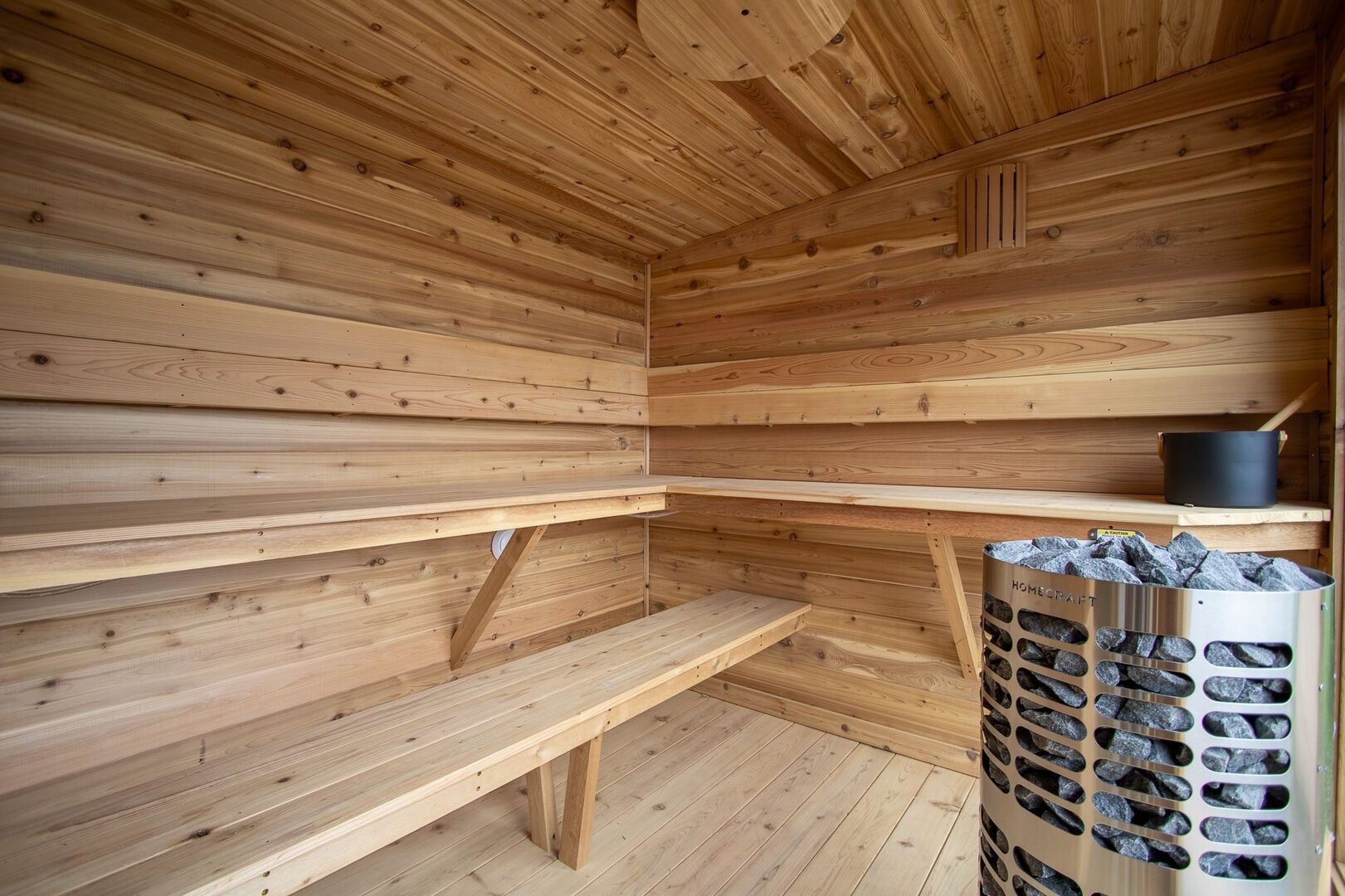 A sauna room with wooden walls, benches, and a stone heater.