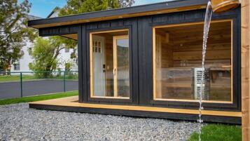 A modern cabin with a wooden exterior, large glass windows, and a water feature.