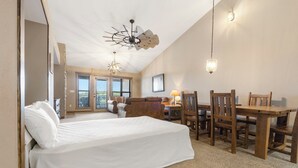A bedroom with a bed, a desk, and chairs, a ceiling fan, and a chandelier.