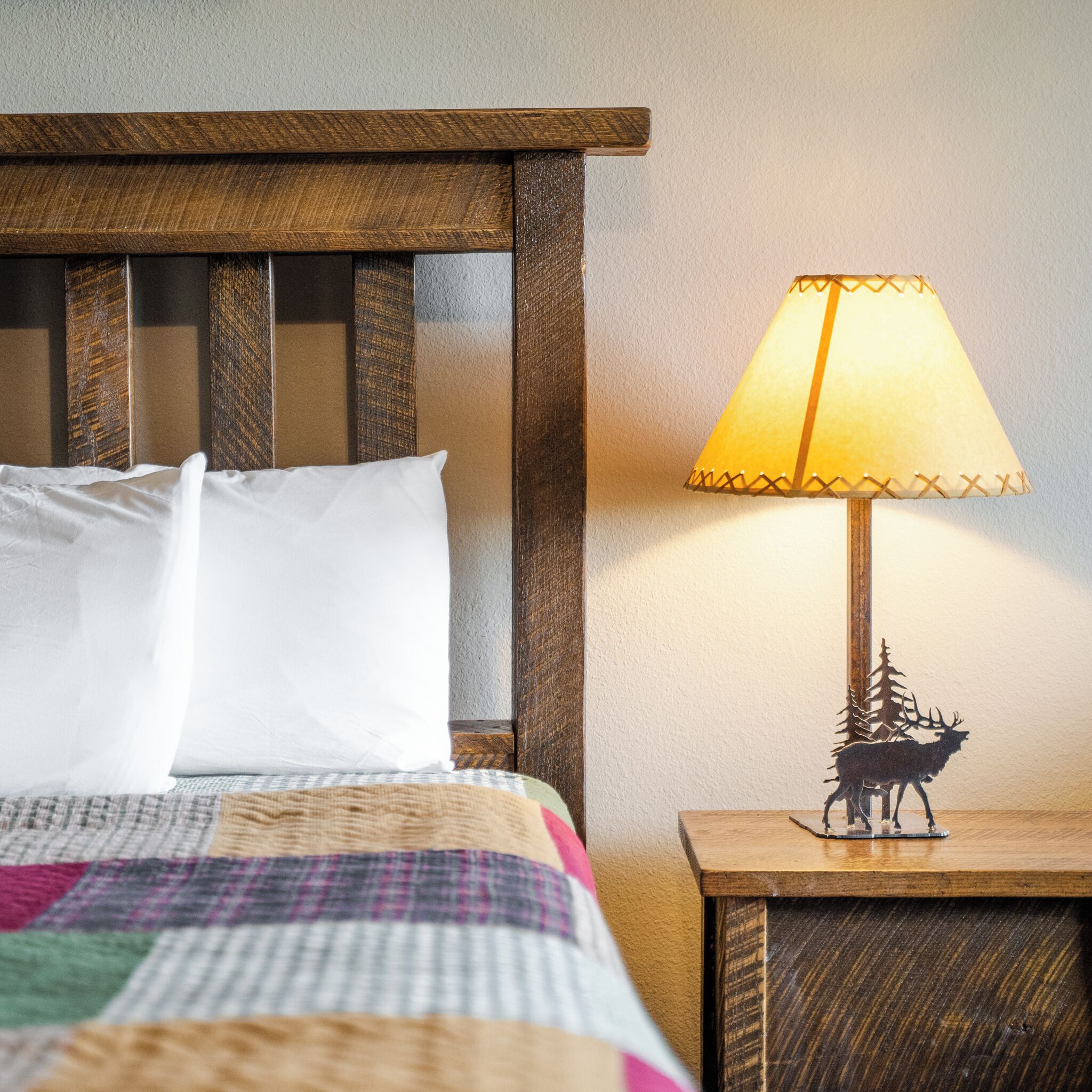 A bed with white pillows and a quilt, a wooden headboard, a nightstand with a lamp, and a decorative elk figurine.