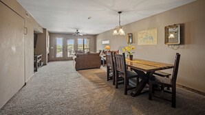 A spacious dining area with a high ceiling, a ceiling fan, and a view of the outdoors through large windows.