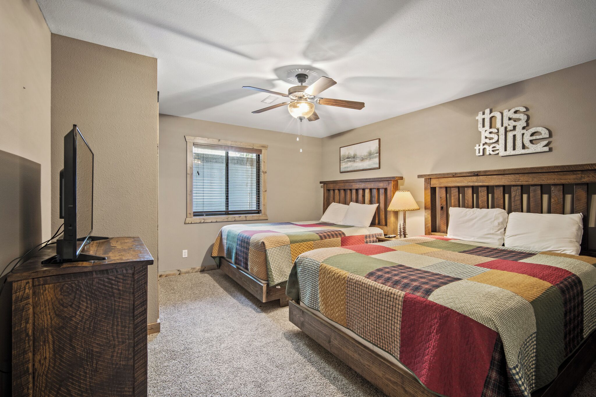 A bedroom with two beds, a ceiling fan, a TV on a wooden cabinet, and a window with blinds.