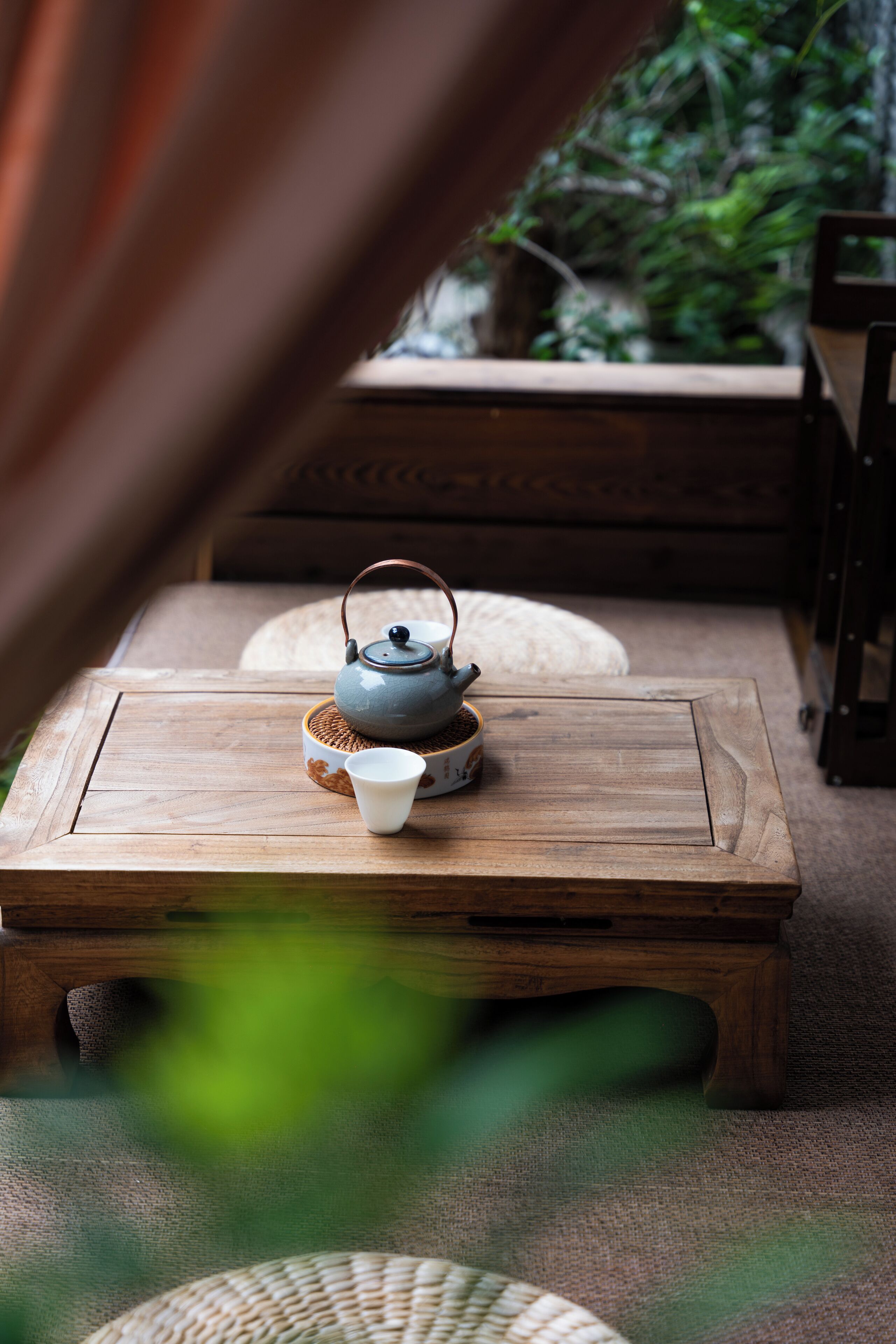 A small wooden table with a teapot and cups, set on a woven mat.