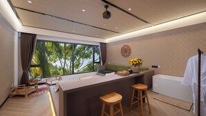 A modern room with a large window, a green sofa, wooden stools, a small table, and a white bathtub. - Yun Guan Shunde Renjia Resort Hotel (Xishuangbanna Dai)