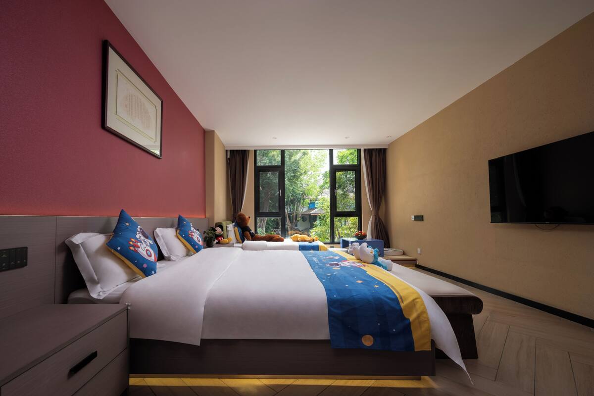 Habitació d'hotel amb un llit gran, televisió i finestra amb vista a arbres.