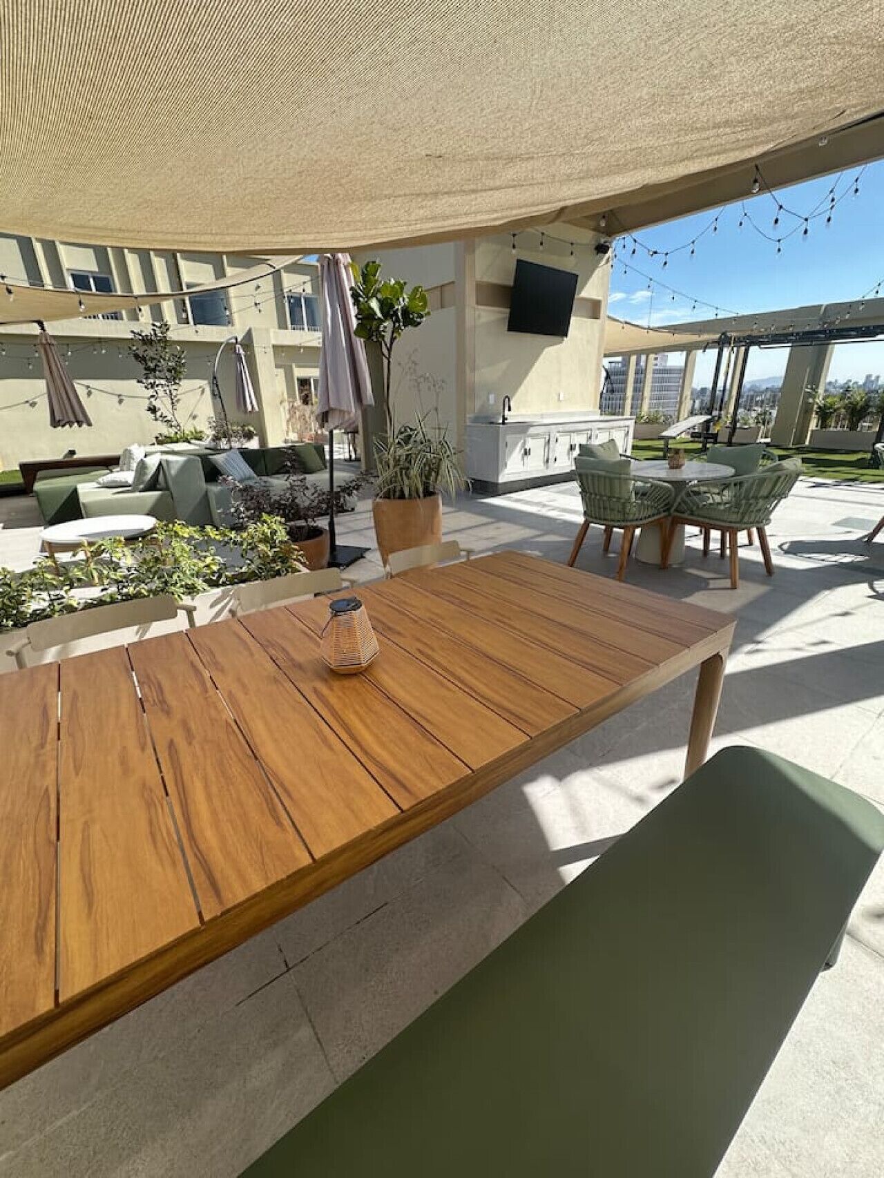 An outdoor patio area with a wooden table, green chairs, and a potted plant.