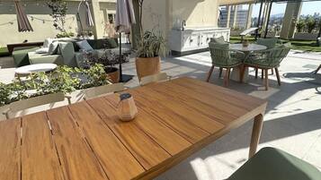 An outdoor patio area with a wooden table, green chairs, and a potted plant.