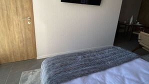 A hotel room with a bed, a television mounted on the wall, a wooden door, and a small table with chairs.