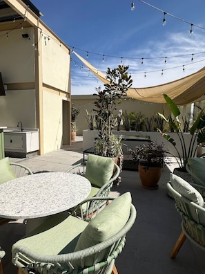 Un espace extérieur aménagé en terrasse, avec une table ronde et des chaises, entouré de plantes en pot et illuminé de guirlandes lumineuses.