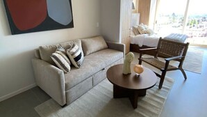 A modern living room with a sofa, a round coffee table, and a chair. There is a large window providing a view of the outside.
