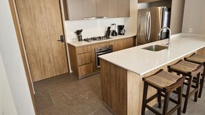 A modern kitchen with wooden cabinets, a stainless steel refrigerator, a gas stove, and a large island with bar stools.