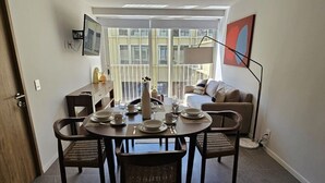 A dining area with a round table set for four, a sofa, a floor lamp, and a large window with blinds.