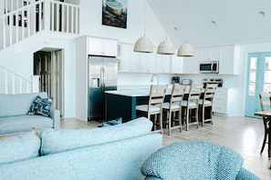 A modern kitchen with white cabinets, a stainless steel refrigerator, and a dining area with wooden chairs and a table.