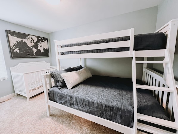 A bunk bed with a grey mattress and white frame in a room with light walls and a world map on the wall.