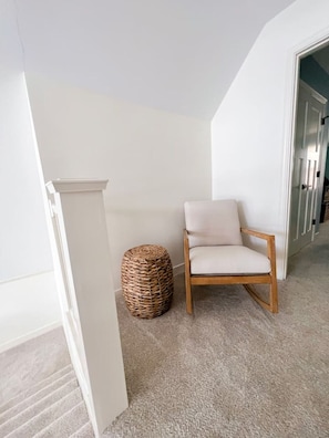 A room with a white wall, a wooden chair, a woven basket, and a carpeted floor.