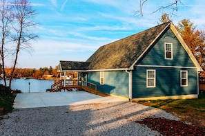 A two-story house with a dock extending into a body of water, surrounded by trees and a clear sky.