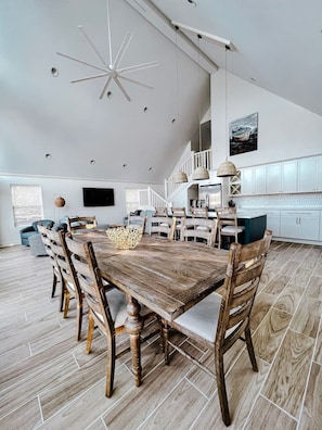 A spacious dining area with a wooden table and chairs, a ceiling fan, and a kitchen in the background.
