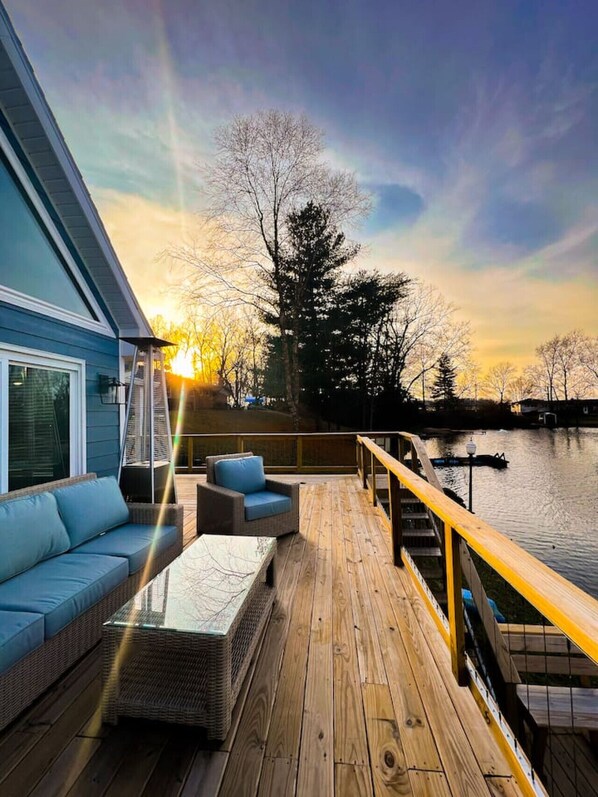 A wooden deck with outdoor furniture, overlooking a body of water and trees.