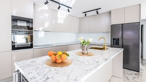 A modern kitchen with a marble countertop, stainless steel appliances, and a central island with a fruit bowl and flowers.