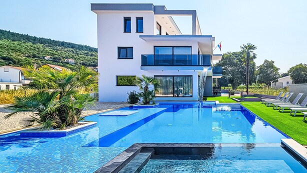 A modern pool area with a clear blue pool, a white building with large windows, and a well-maintained lawn with lounge chairs.