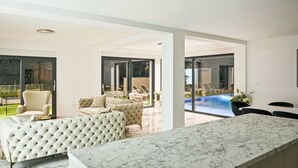 A modern living room with a marble countertop, comfortable seating, and a view of an outdoor pool area.