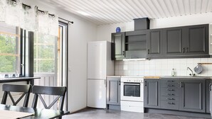 A modern kitchen with dark cabinets, a white refrigerator, and a stove. There is a window with curtains and a table with chairs. - Skärvudde Villan by Interhome (Kalvsvik)